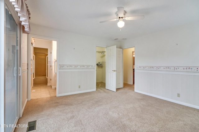 unfurnished bedroom with a spacious closet, ceiling fan, ensuite bathroom, light carpet, and a closet