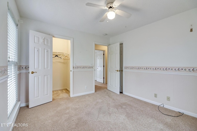 unfurnished bedroom featuring ceiling fan, a spacious closet, light carpet, and a closet