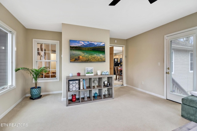 living area featuring ceiling fan, a healthy amount of sunlight, and light carpet