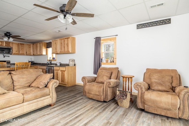 living room featuring ceiling fan, hardwood / wood-style flooring, a drop ceiling, and sink