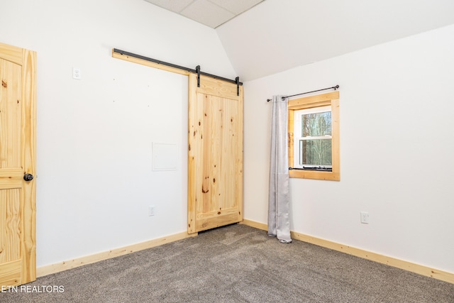 empty room with carpet flooring, a barn door, and lofted ceiling