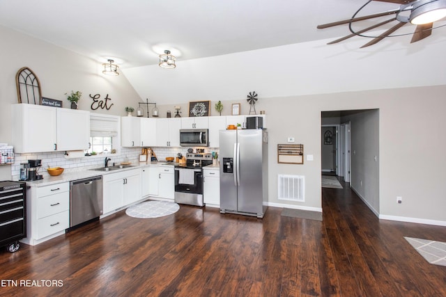 kitchen with lofted ceiling, backsplash, sink, appliances with stainless steel finishes, and white cabinetry