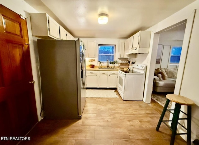 kitchen with white electric range, white cabinetry, stainless steel refrigerator, and sink