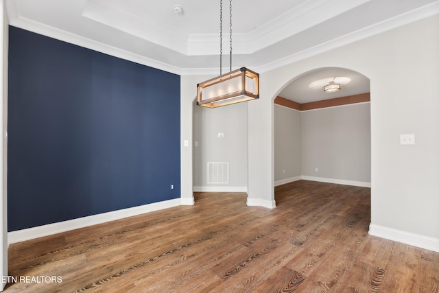 unfurnished room featuring a raised ceiling, hardwood / wood-style floors, and ornamental molding