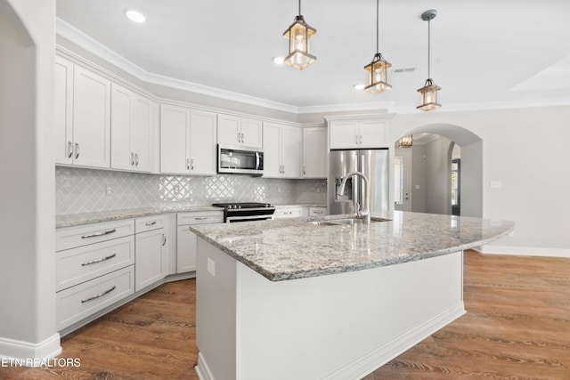 kitchen featuring stainless steel appliances, light stone counters, an island with sink, pendant lighting, and white cabinets