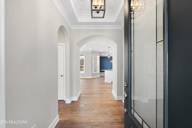 corridor featuring hardwood / wood-style flooring, a raised ceiling, and ornamental molding