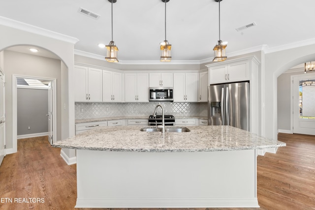 kitchen with white cabinetry, stainless steel appliances, tasteful backsplash, light stone counters, and a center island with sink