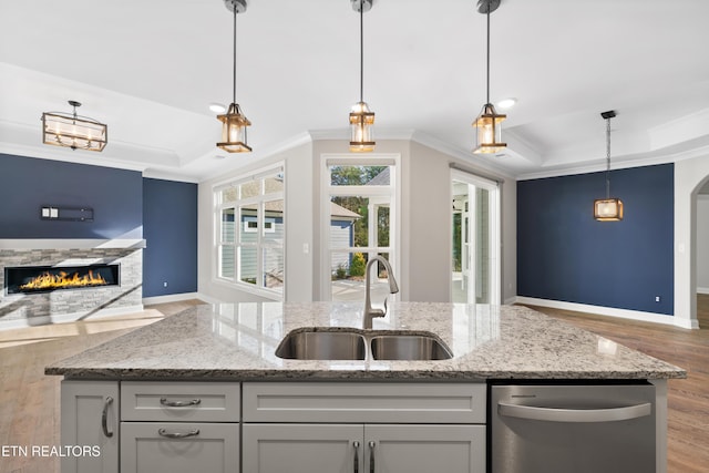 kitchen with gray cabinetry, light stone counters, sink, and an island with sink