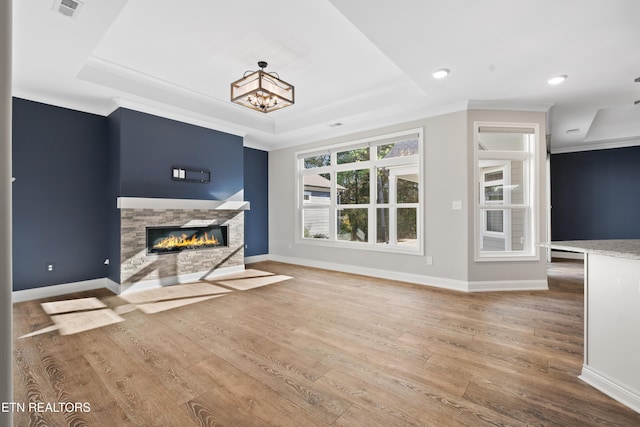 unfurnished living room with a raised ceiling, wood-type flooring, crown molding, and a chandelier