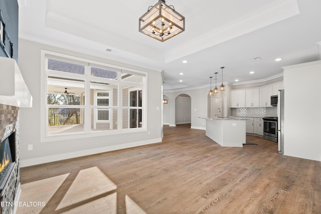 living room with a tray ceiling, crown molding, light wood-type flooring, and a brick fireplace