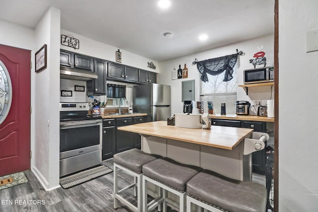 kitchen featuring dark wood-type flooring, sink, appliances with stainless steel finishes, butcher block countertops, and a breakfast bar area