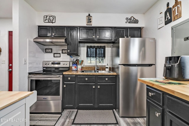 kitchen featuring appliances with stainless steel finishes, light wood-type flooring, sink, butcher block counters, and range hood