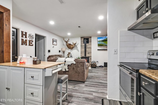 kitchen with a wood stove, backsplash, stainless steel range with electric cooktop, butcher block countertops, and wood-type flooring