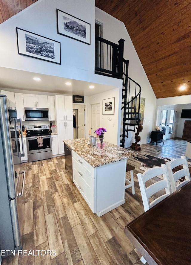 kitchen with appliances with stainless steel finishes, light stone countertops, white cabinets, a kitchen island, and wooden ceiling