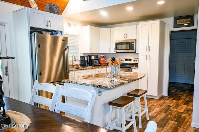 kitchen featuring stainless steel appliances, a breakfast bar, sink, dark stone countertops, and white cabinets