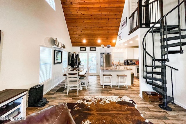 kitchen with a breakfast bar, stainless steel refrigerator, a high ceiling, wood-type flooring, and white cabinets