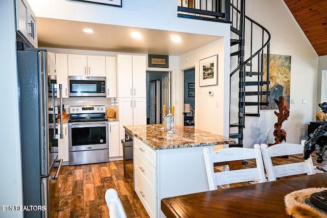 kitchen with dark wood-type flooring, stainless steel appliances, white cabinets, dark stone counters, and backsplash