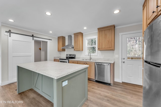 kitchen featuring wall chimney range hood, a barn door, ornamental molding, appliances with stainless steel finishes, and a kitchen island