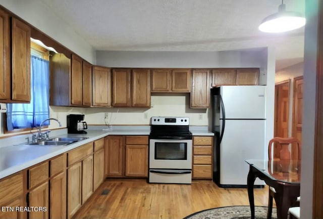 kitchen with sink, stainless steel appliances, decorative light fixtures, and light wood-type flooring