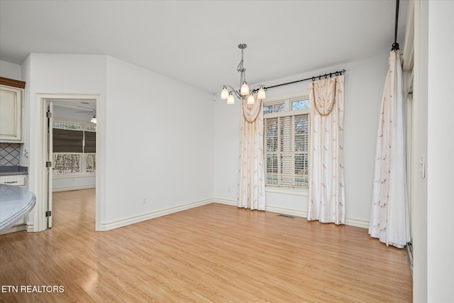 unfurnished dining area featuring plenty of natural light, light wood-type flooring, and ceiling fan with notable chandelier