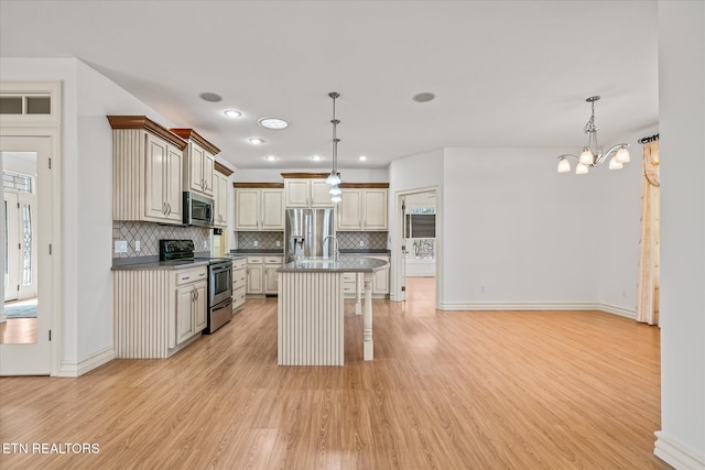 kitchen featuring pendant lighting, a kitchen bar, a kitchen island with sink, appliances with stainless steel finishes, and light wood-type flooring