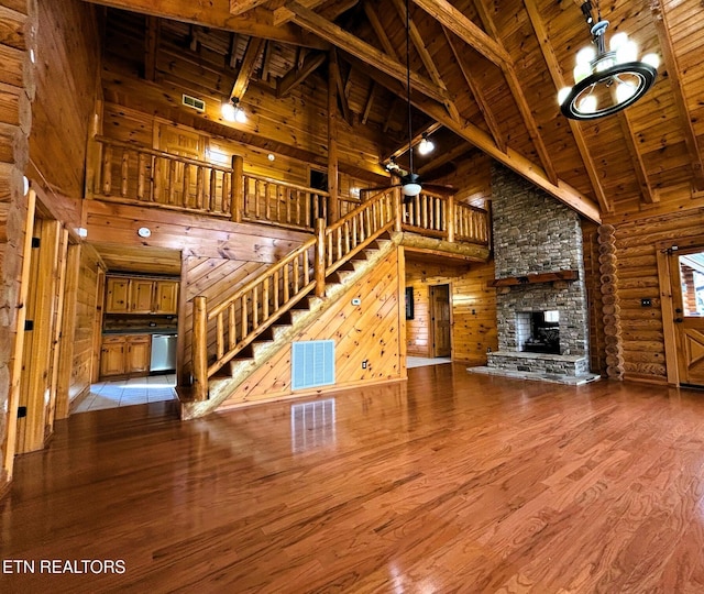 unfurnished living room featuring rustic walls, a stone fireplace, beamed ceiling, high vaulted ceiling, and wood ceiling