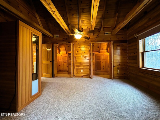 carpeted spare room featuring vaulted ceiling with beams, ceiling fan, wooden ceiling, and rustic walls