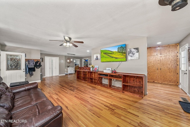 living room with a textured ceiling, light hardwood / wood-style floors, and ceiling fan