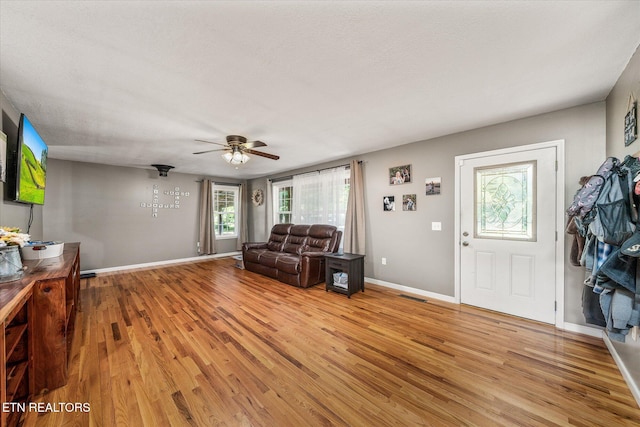 living room featuring a textured ceiling, light wood-type flooring, and ceiling fan