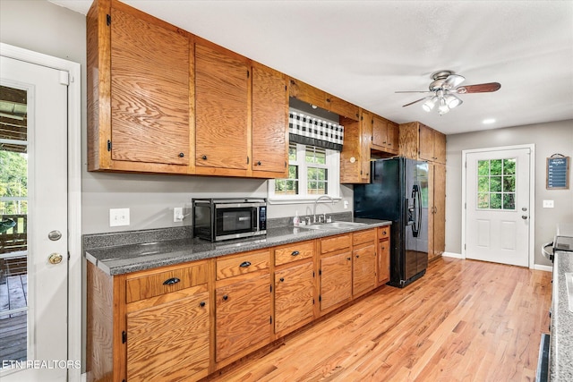 kitchen with black fridge with ice dispenser, light hardwood / wood-style flooring, ceiling fan, and sink