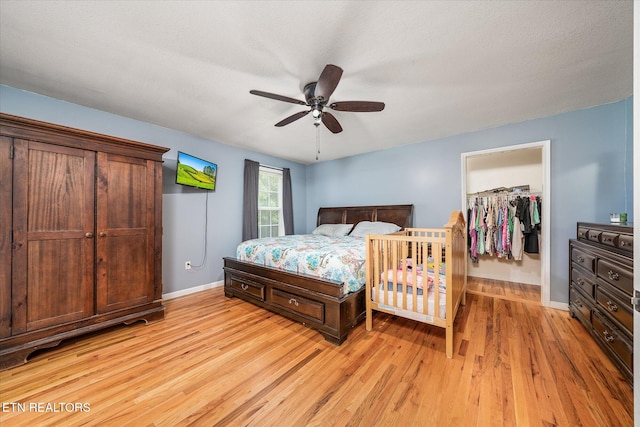 bedroom with a spacious closet, ceiling fan, a textured ceiling, a closet, and light wood-type flooring