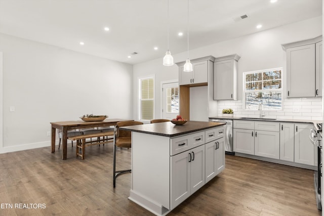 kitchen with a sink, a kitchen island, tasteful backsplash, dark countertops, and decorative light fixtures