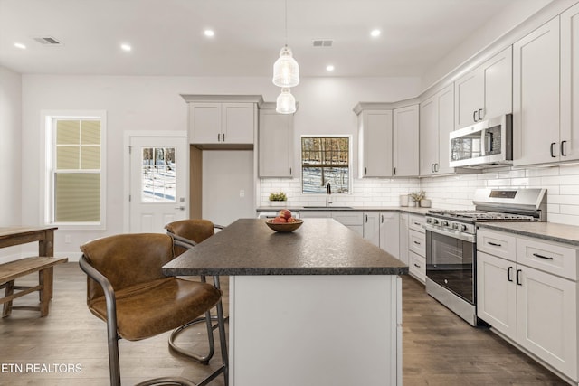 kitchen with sink, appliances with stainless steel finishes, hanging light fixtures, dark hardwood / wood-style floors, and a center island