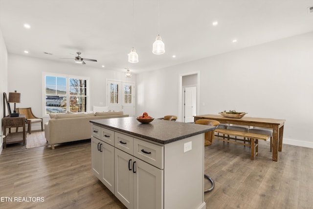 kitchen with open floor plan, a center island, dark countertops, dark wood finished floors, and decorative light fixtures