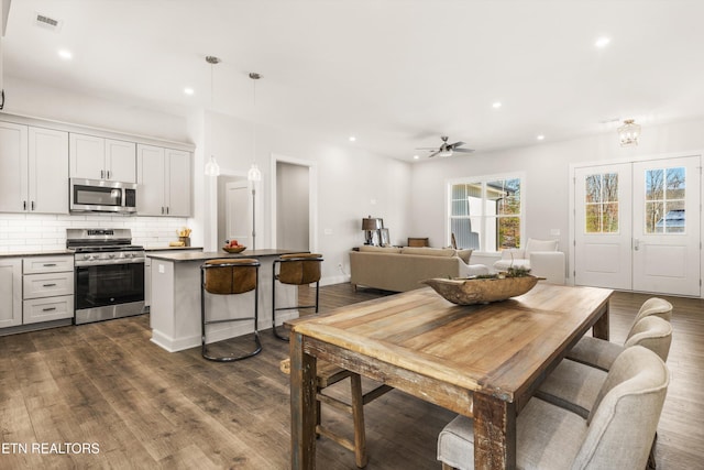 kitchen with dark wood-type flooring, ceiling fan, appliances with stainless steel finishes, backsplash, and decorative light fixtures