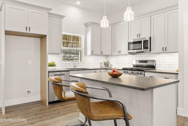 kitchen featuring a center island, decorative light fixtures, dark countertops, appliances with stainless steel finishes, and a sink