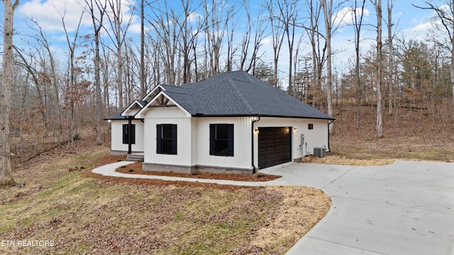 exterior space featuring cooling unit, concrete driveway, roof with shingles, and an attached garage