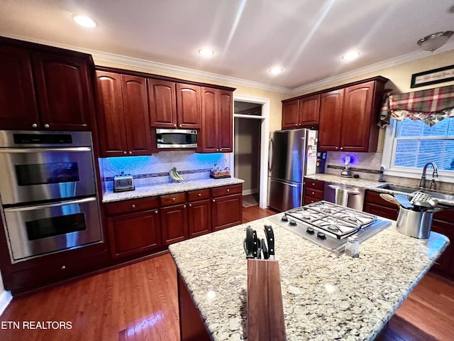 kitchen featuring sink, light stone counters, backsplash, appliances with stainless steel finishes, and ornamental molding