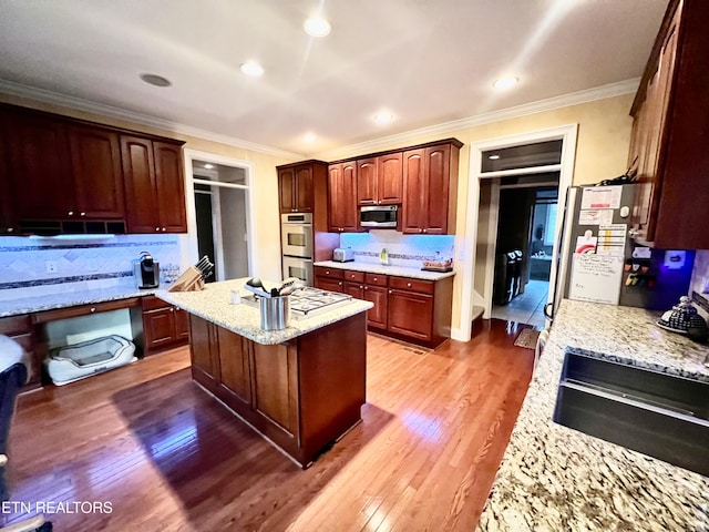 kitchen featuring a kitchen island, light stone counters, ornamental molding, and appliances with stainless steel finishes