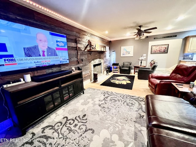 living room featuring ceiling fan, crown molding, wood-type flooring, a stone fireplace, and wood walls