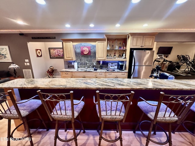 kitchen featuring light stone countertops, a kitchen bar, stainless steel refrigerator, and sink