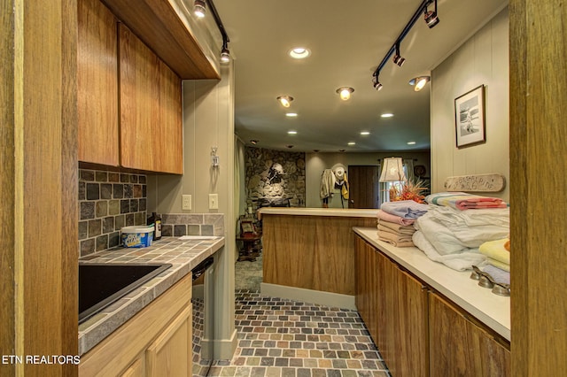 kitchen featuring decorative backsplash, kitchen peninsula, track lighting, stainless steel dishwasher, and sink