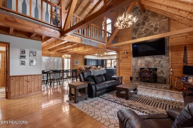 living room featuring a stone fireplace, high vaulted ceiling, a notable chandelier, wood walls, and hardwood / wood-style flooring