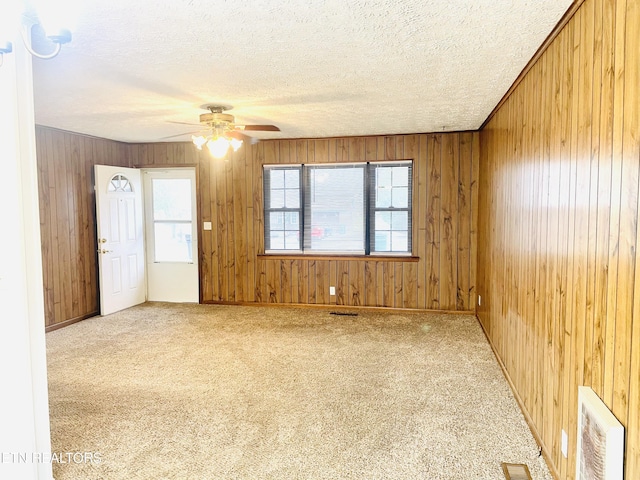 carpeted empty room with a textured ceiling, ceiling fan, and wood walls