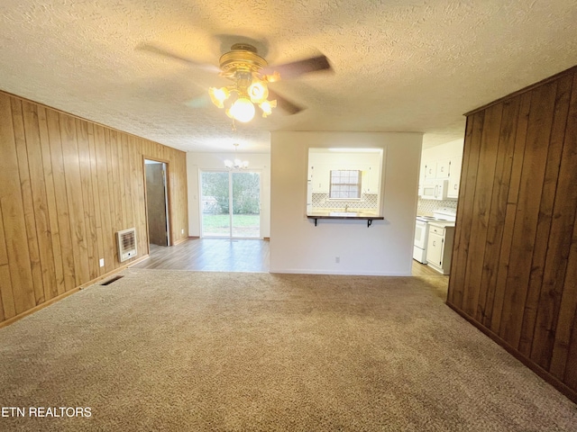 unfurnished living room featuring ceiling fan with notable chandelier, wooden walls, carpet flooring, a textured ceiling, and heating unit