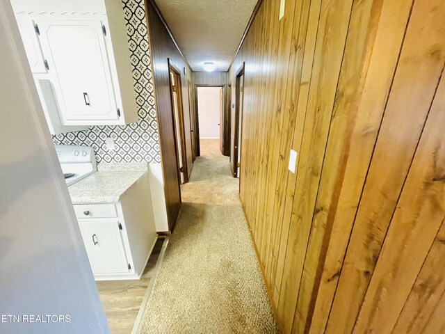 hall featuring wood walls, light carpet, and a textured ceiling