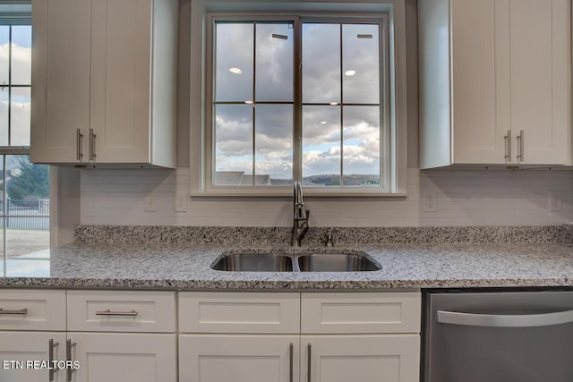 kitchen featuring backsplash, sink, stainless steel dishwasher, light stone countertops, and white cabinetry