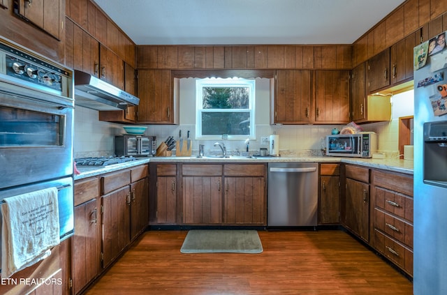 kitchen with appliances with stainless steel finishes, tasteful backsplash, dark wood-type flooring, and sink