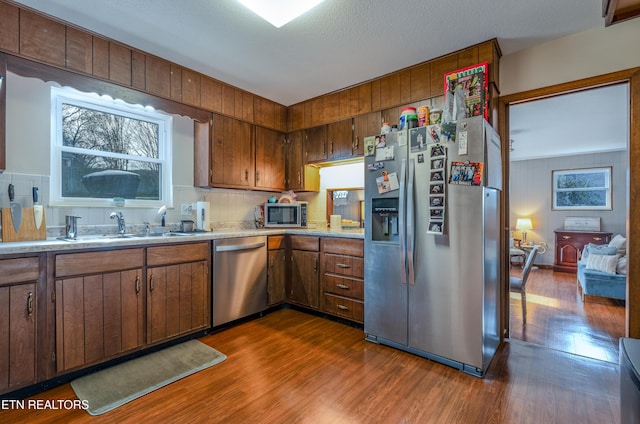 kitchen with backsplash, a textured ceiling, stainless steel appliances, dark wood-type flooring, and sink