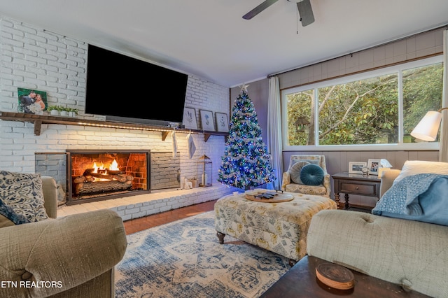 living room with ceiling fan, wood-type flooring, brick wall, and a brick fireplace